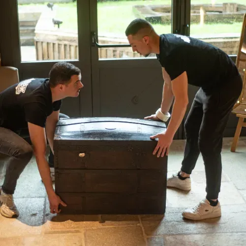 Deux déménageurs Apex portent un meuble volumineux au sortir d’un local professionnel